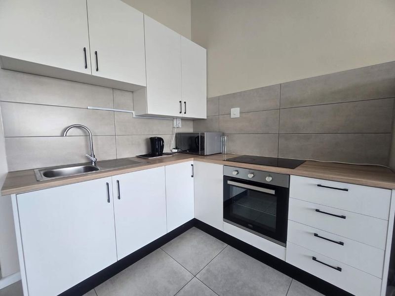 Modern kitchen featuring white cabinetry, wood-look laminate countertops, tiled backsplash, and integrated stainless steel appliances including an oven and hob.