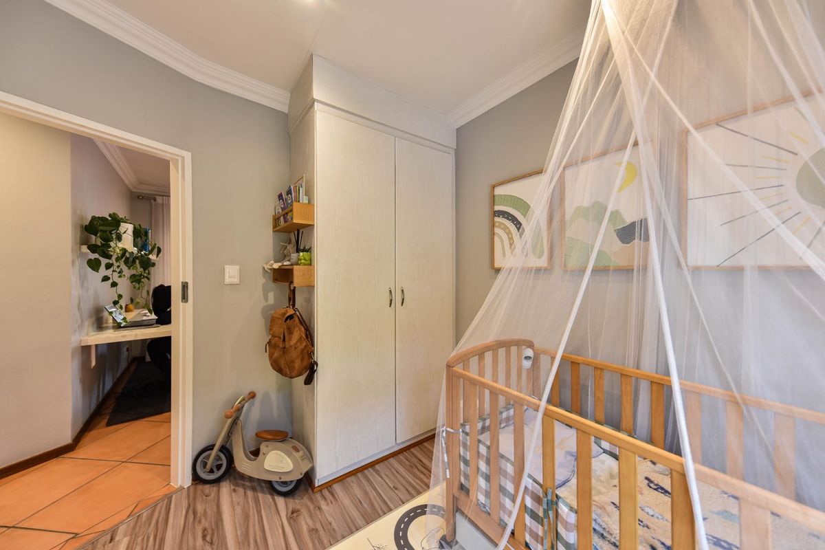 A well-maintained bedroom featuring built-in wardrobes, crown molding, and durable laminate flooring, with a view into an adjacent room.
