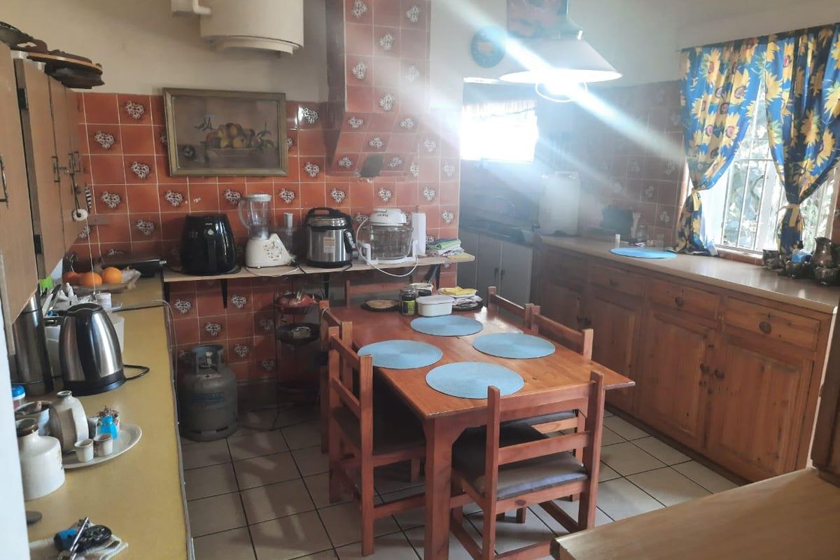 A dated kitchen featuring traditional wooden cabinetry, tiled splashbacks, and a central dining area with tiled flooring.