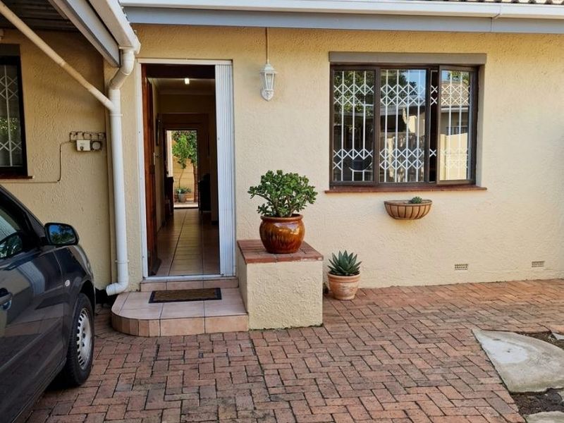 Front entrance of the townhouse featuring a brick-paved driveway, security-barred windows, and a covered entryway.