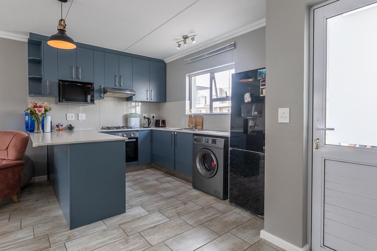 Modern kitchen featuring blue cabinetry, stone countertops, integrated oven, gas hob, extractor fan, and tiled flooring with direct access to the exterior.