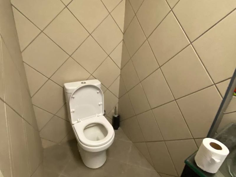 A compact bathroom featuring tiled walls and flooring, equipped with a standard toilet and a vanity unit.