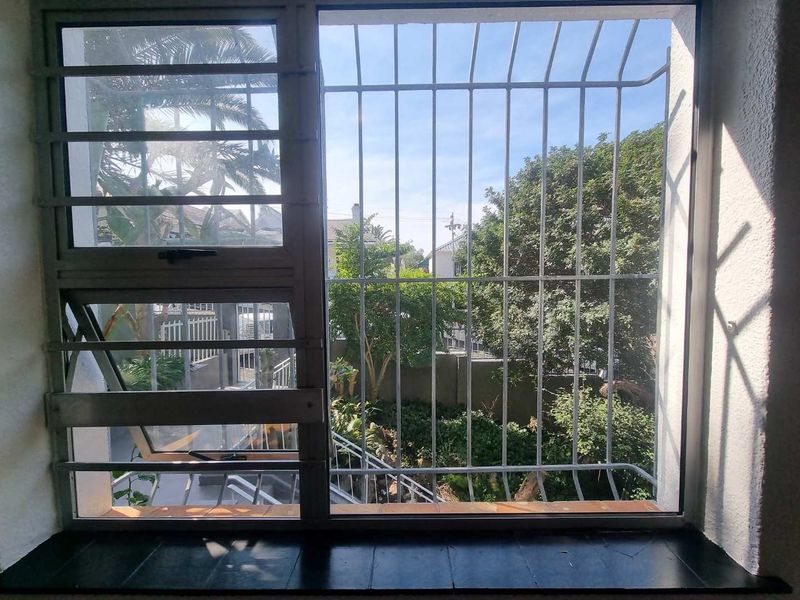 A view from an interior window looking out onto a garden area, featuring security bars and a tiled window sill.