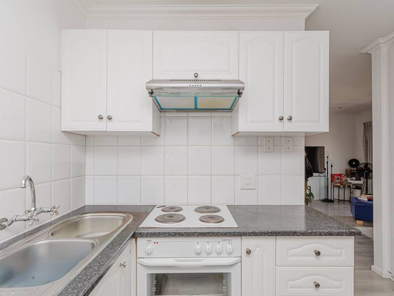 A functional kitchen featuring white cabinetry, a tiled splashback, integrated electric hob, oven, extractor fan, and a stainless steel sink with a mixer tap.