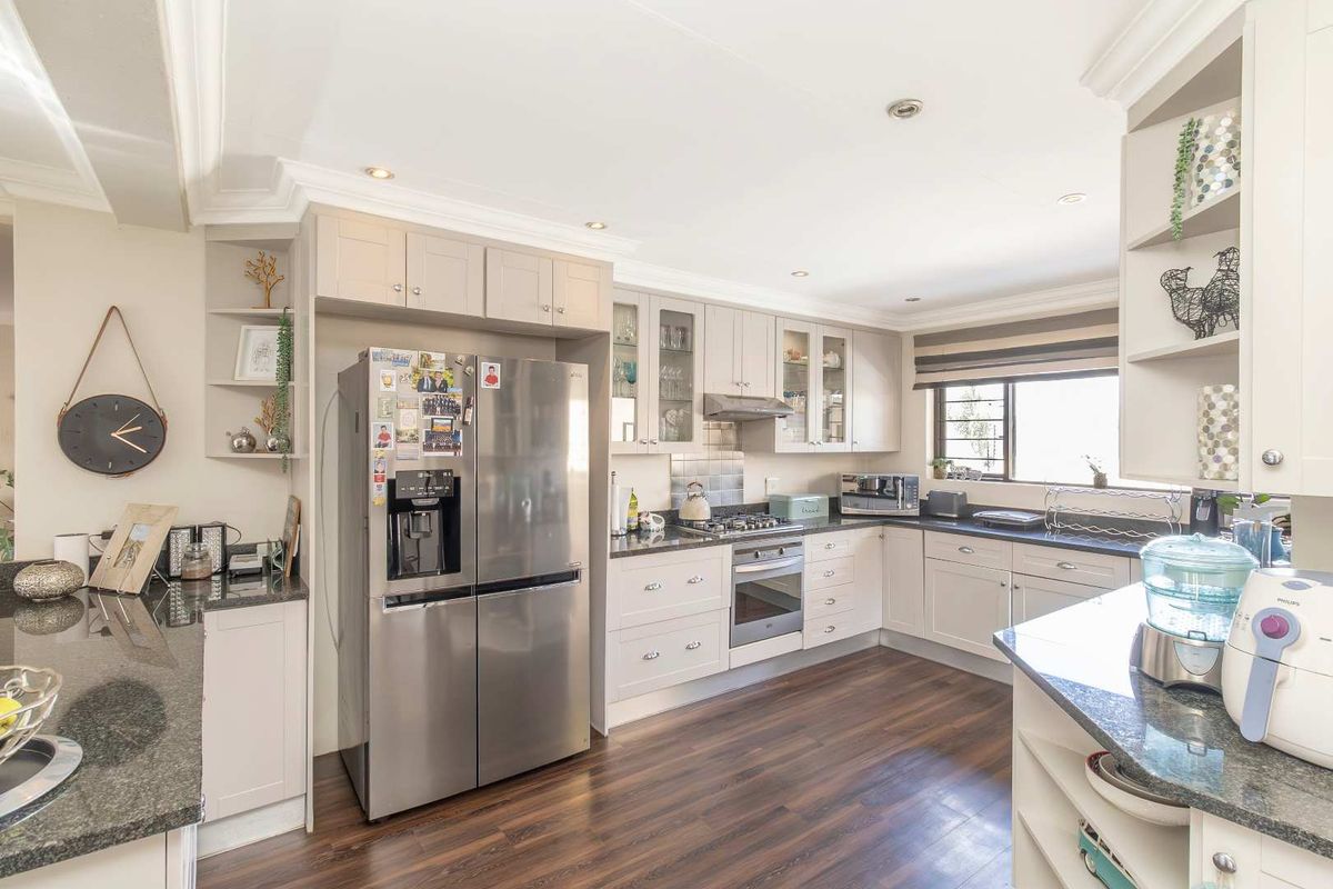 A well-appointed kitchen featuring shaker-style cabinetry, granite countertops, a built-in oven, gas hob, and an integrated extractor fan with wood-look flooring.