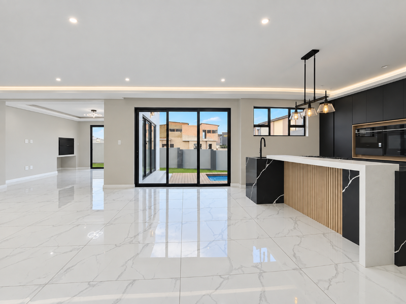 Modern open-plan living and kitchen area featuring high-end marble-look flooring, sleek black cabinetry, integrated appliances, and seamless access to the outdoor patio and pool.