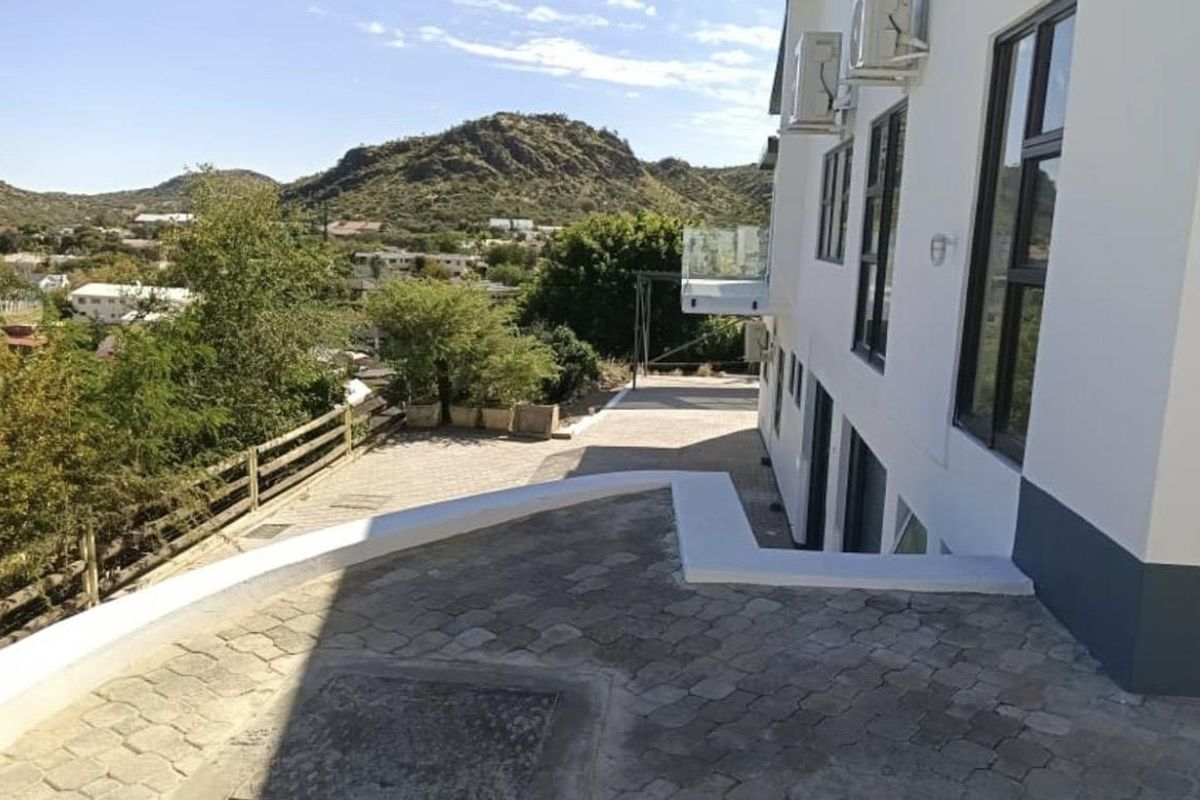 Exterior view of the property featuring paved outdoor areas, a glass-railed balcony, and scenic mountain views.
