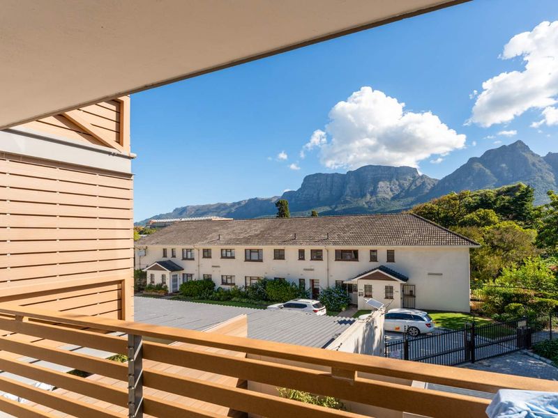 A covered balcony featuring a modern timber-look balustrade, offering elevated views of the surrounding apartment complex and mountain range.