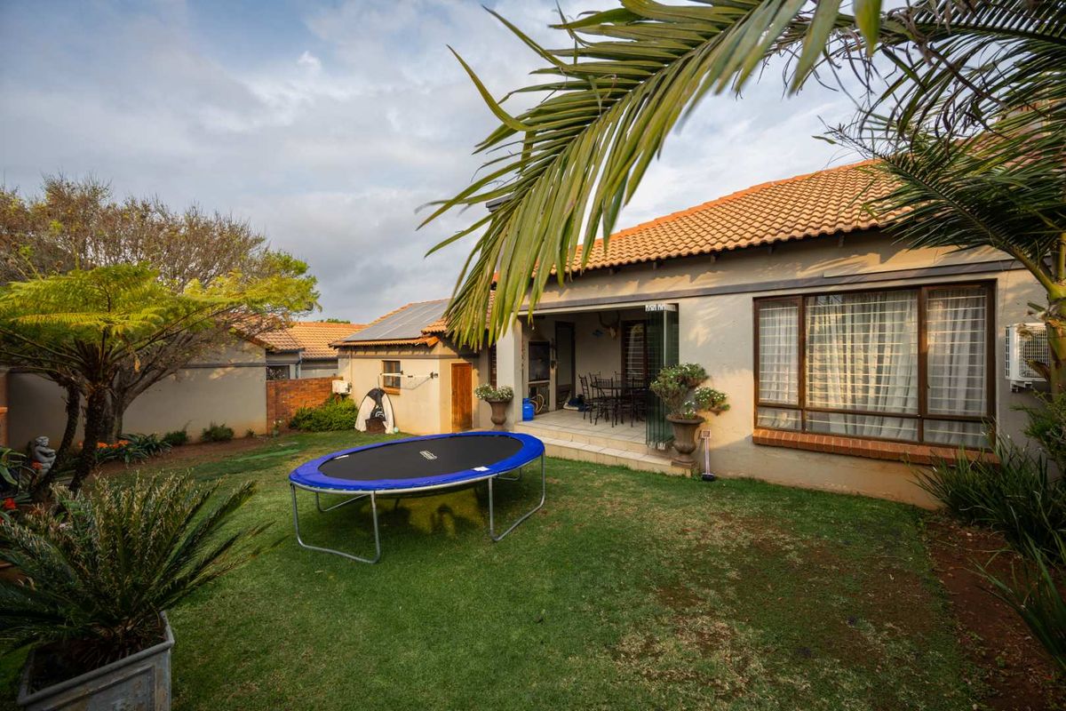 A rear view of the cluster home featuring a well-maintained lawn, a covered patio area, and solar panels installed on the tiled roof.