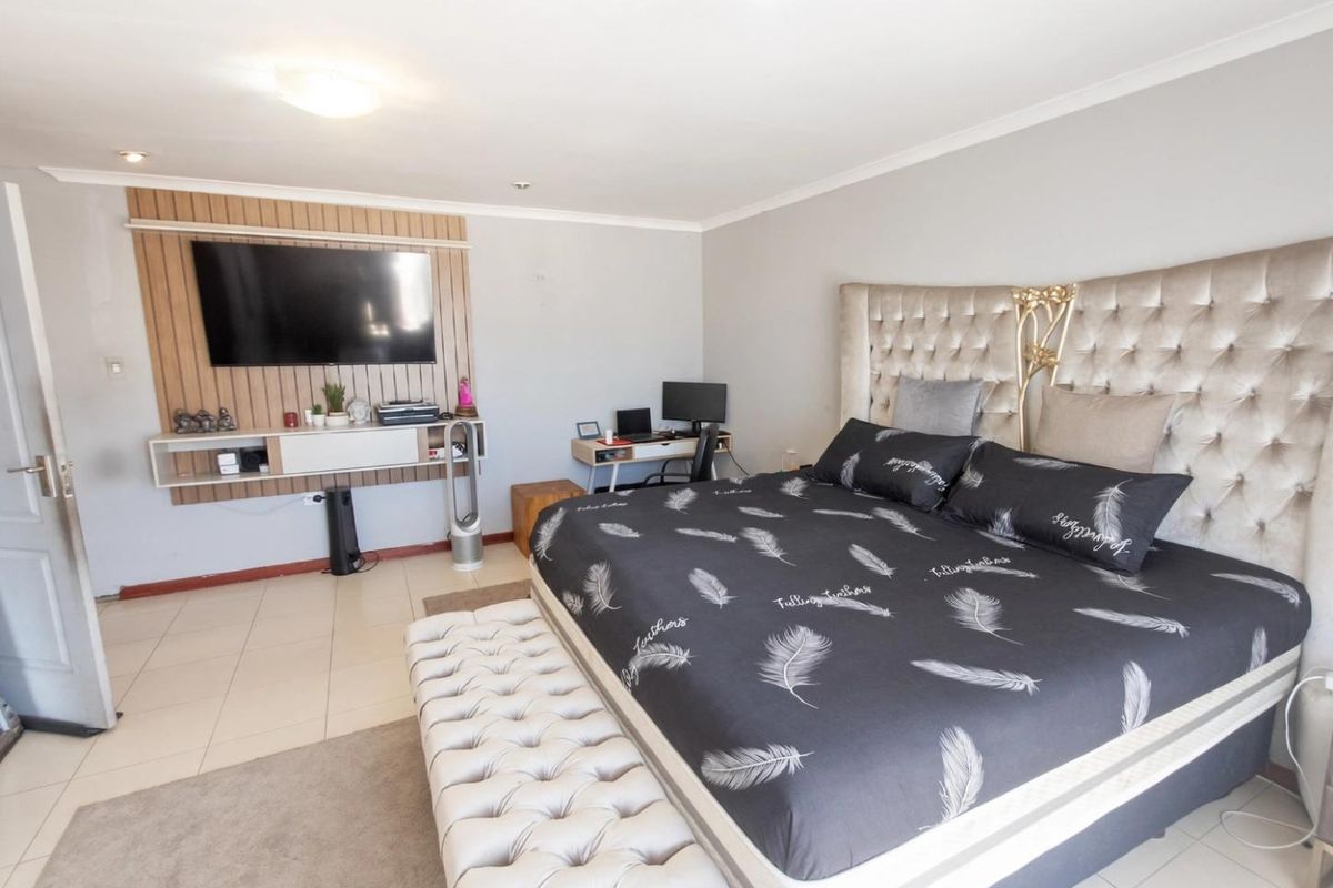 Spacious bedroom featuring tiled flooring, coved ceilings, and a custom built-in wall paneling unit for media storage.