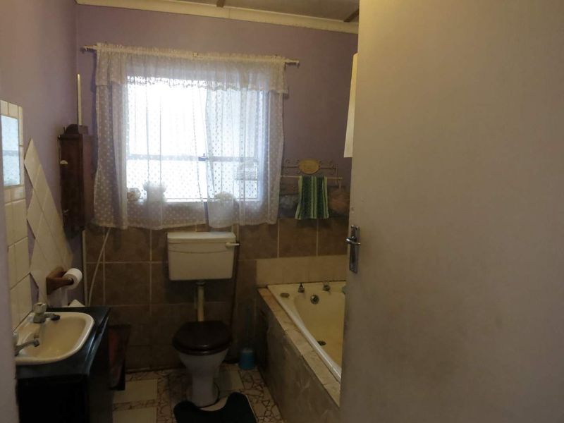 A dated bathroom featuring a built-in bathtub, toilet, and pedestal basin with tiled splashbacks, requiring modernization to improve its overall condition and appeal.