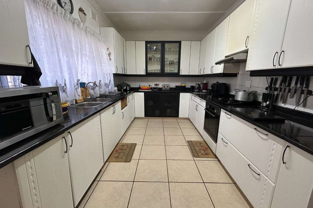 A functional galley-style kitchen featuring white cabinetry, black granite countertops, built-in oven, gas hob, and tiled flooring.