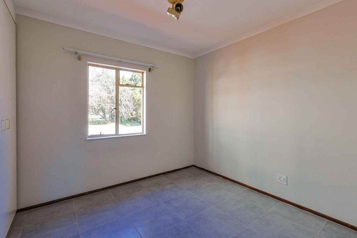 A bright, empty bedroom featuring neutral wall tones, tiled flooring, and a built-in wardrobe, offering a clean canvas for personalization.