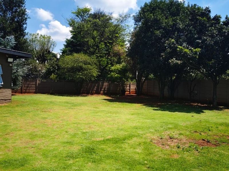 A spacious, private backyard featuring a large lawn, mature trees, and secure precast concrete boundary walls.