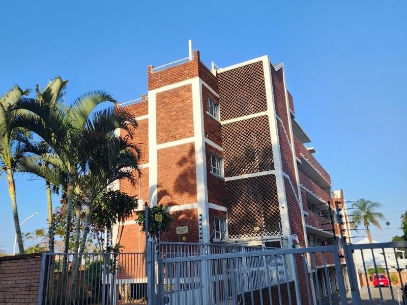 Exterior view of a multi-story brick apartment building featuring secure gated access, perimeter fencing, and established palm trees.