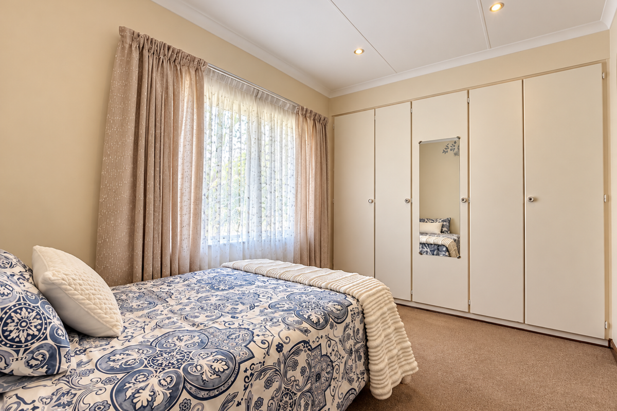 A well-maintained bedroom featuring neutral walls, carpeted flooring, recessed lighting, and extensive built-in wardrobe storage with a central mirror panel.