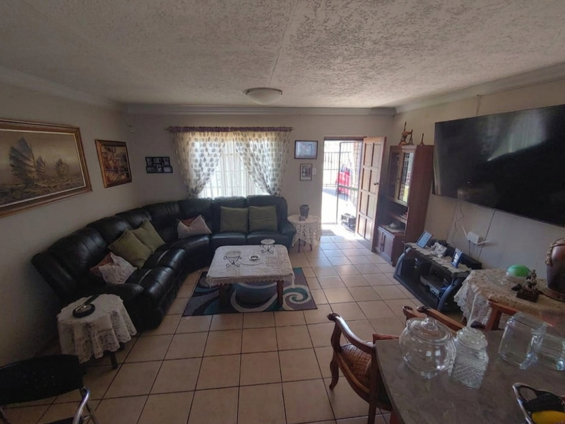 A living room featuring tiled flooring, coving, and direct access to the exterior through a security gate and timber door.