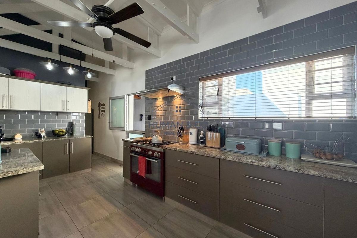 Modern kitchen featuring grey subway tile backsplash, granite countertops, ample cabinetry, gas stove, and exposed white timber ceiling beams with a ceiling fan.