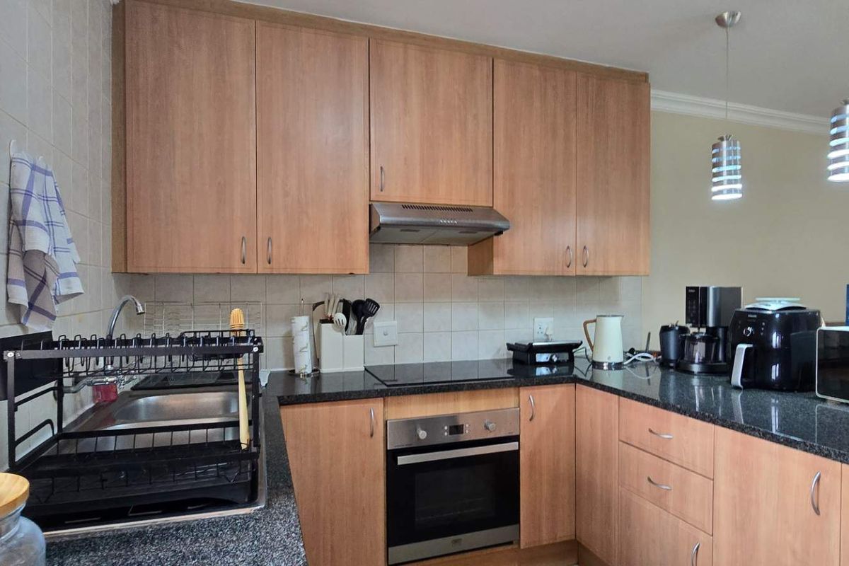 A functional kitchen featuring wood-finish cabinetry, granite countertops, a built-in oven, an electric hob, and an integrated extractor fan.