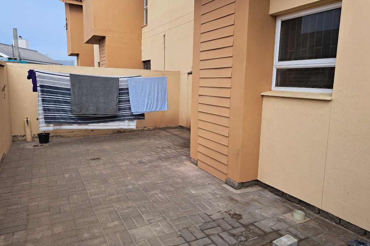 A paved rear courtyard area featuring a boundary wall and exterior building access, suitable for outdoor utility use.