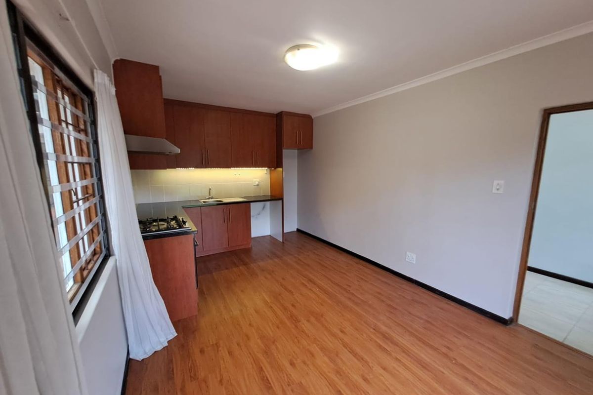 A clean, functional kitchen featuring wood-finish cabinetry, a gas hob, extractor fan, and durable laminate flooring, offering a bright and well-maintained workspace.