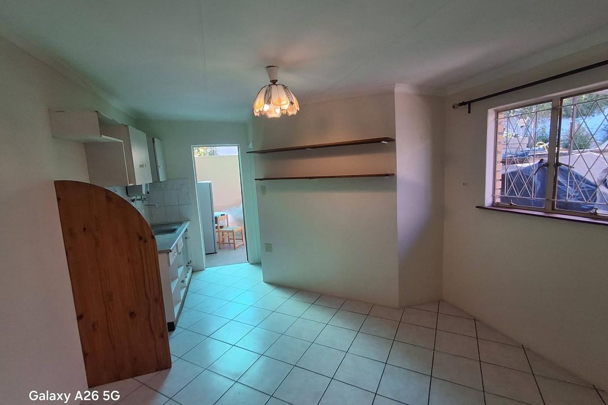 A compact kitchen area featuring tiled flooring, built-in cabinetry, and wall-mounted shelving, with direct access to an outdoor space.