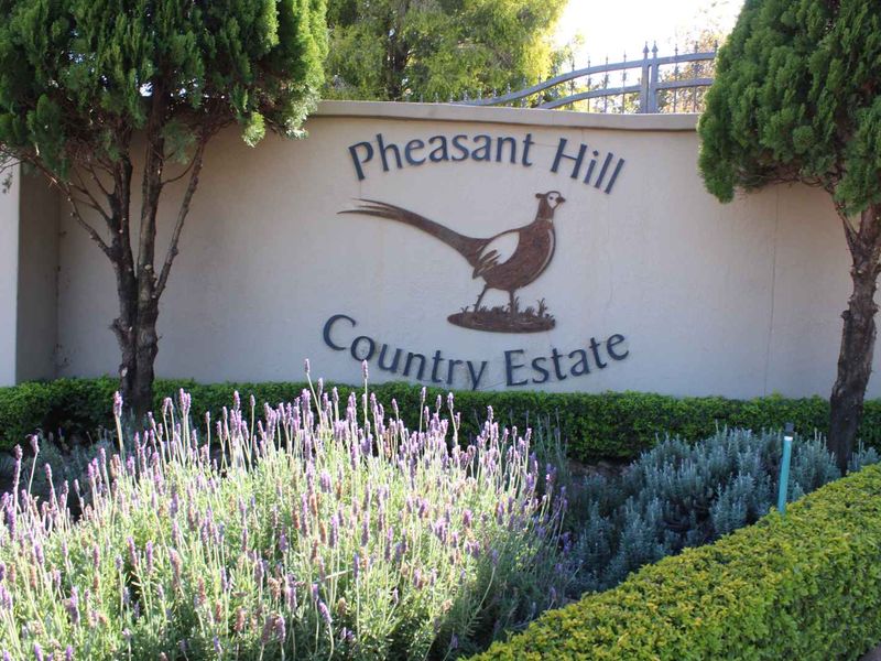 The entrance signage and landscaped boundary wall of Pheasant Hill Country Estate, featuring established trees and manicured garden beds.