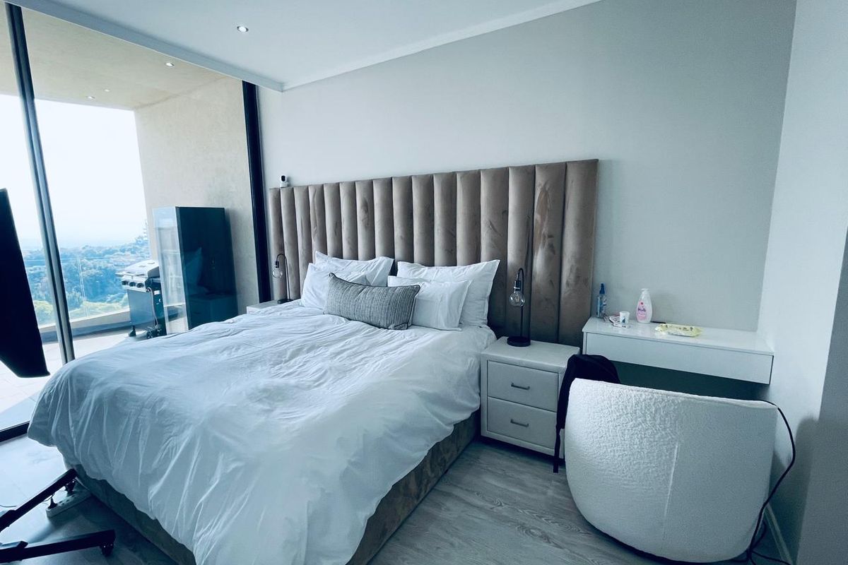 Modern bedroom featuring laminate flooring, recessed lighting, and large floor-to-ceiling glass doors providing access to an outdoor balcony area.