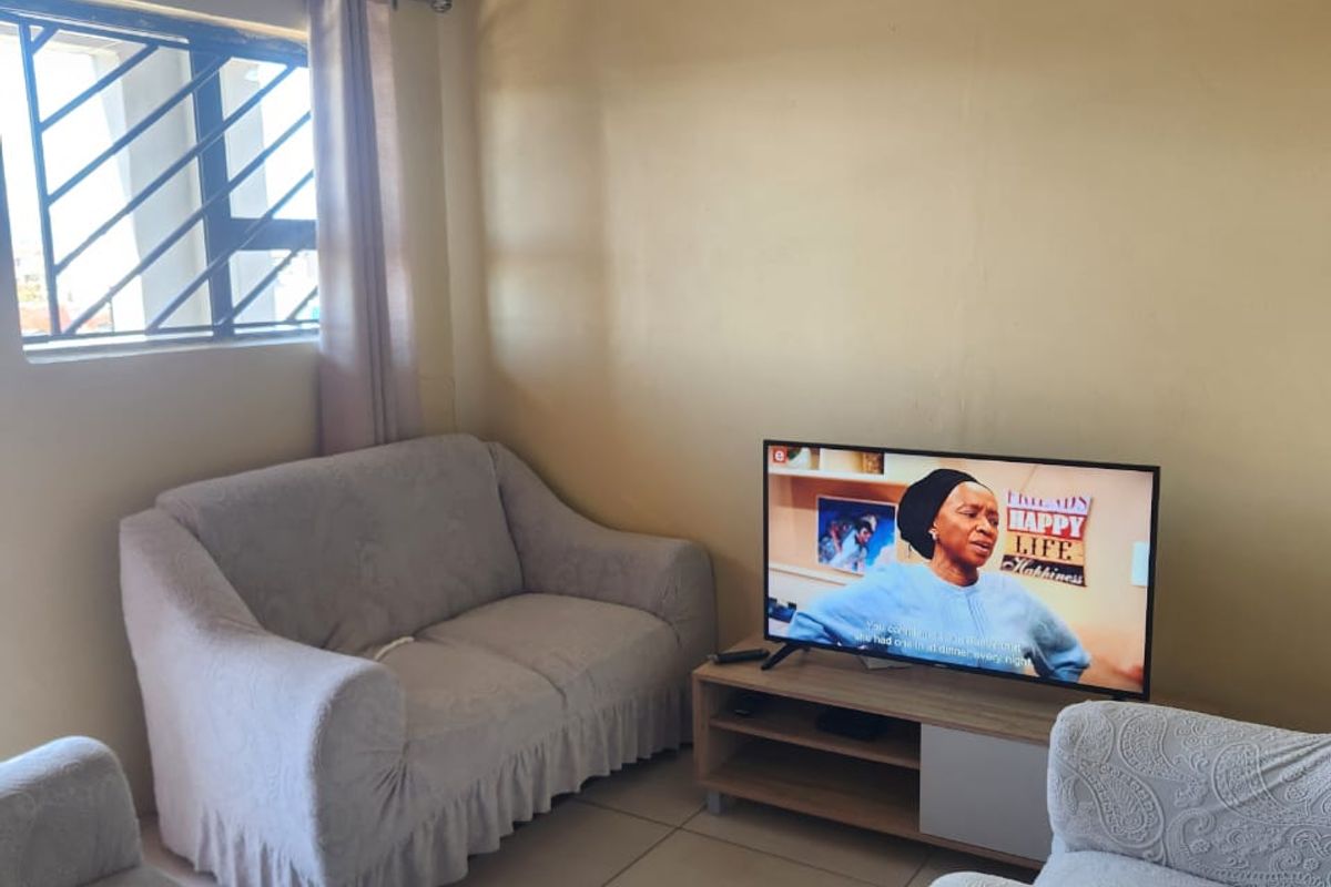 A modest living room featuring tiled floors, security window bars, and an unfinished exposed ceiling, offering potential for renovation and aesthetic improvement.