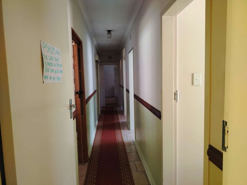 A long residential hallway featuring tiled flooring and multiple doorways, showing signs of wear and requiring cosmetic updates to the walls and ceiling.