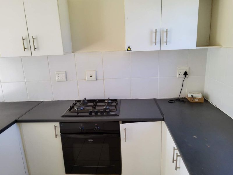 A functional kitchen area featuring white cabinetry, dark laminate countertops, a built-in oven, and a gas hob with a tiled backsplash.