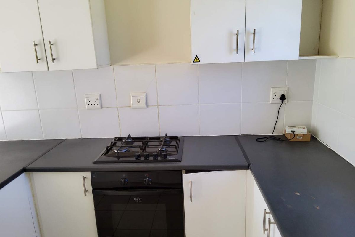 A functional kitchen area featuring white cabinetry, dark laminate countertops, a built-in oven, and a gas hob with a tiled backsplash.