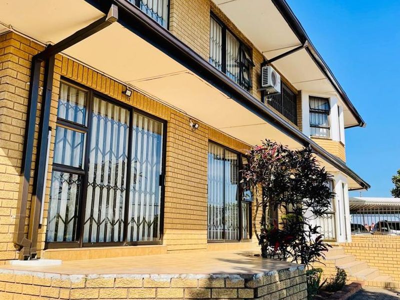 A well-maintained brick exterior featuring a paved driveway, tiled patio area, and secure aluminium-framed windows with security gates.