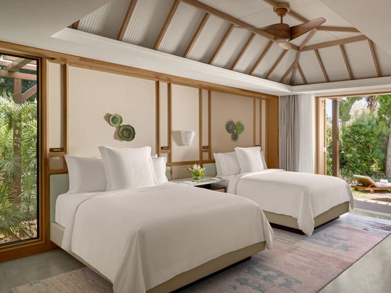 Spacious bedroom featuring a vaulted ceiling with exposed timber beams, polished concrete floors, and large sliding glass doors opening to a private garden area.