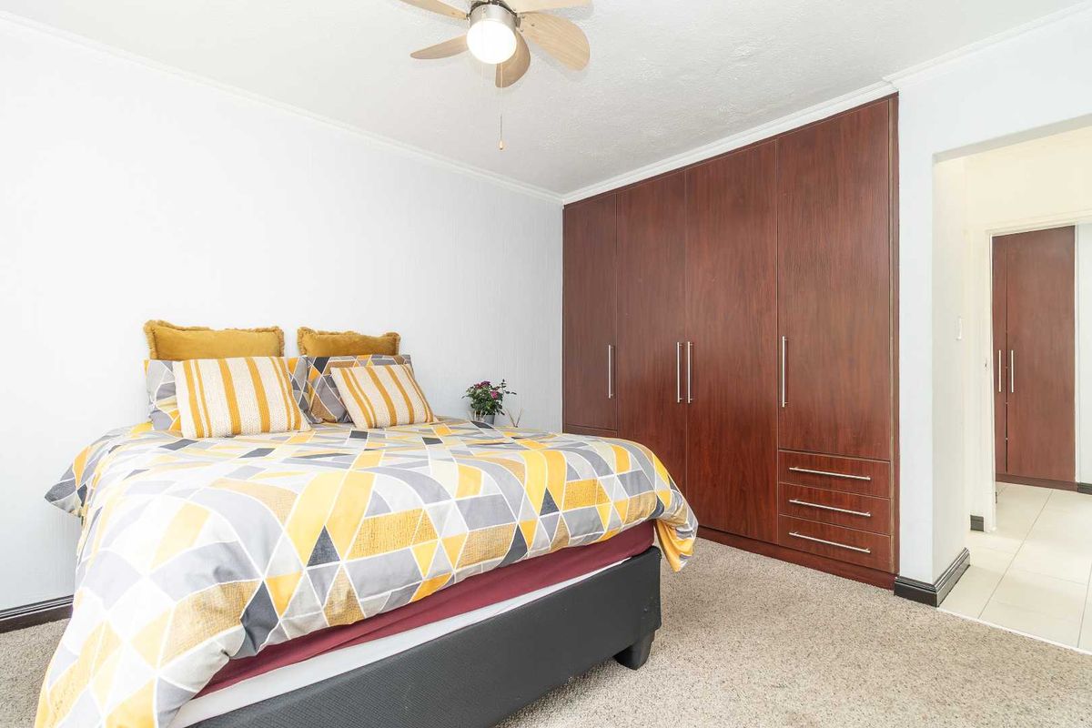 A bedroom featuring built-in wooden cupboards, a ceiling fan, and carpeted flooring, with an adjacent hallway visible.