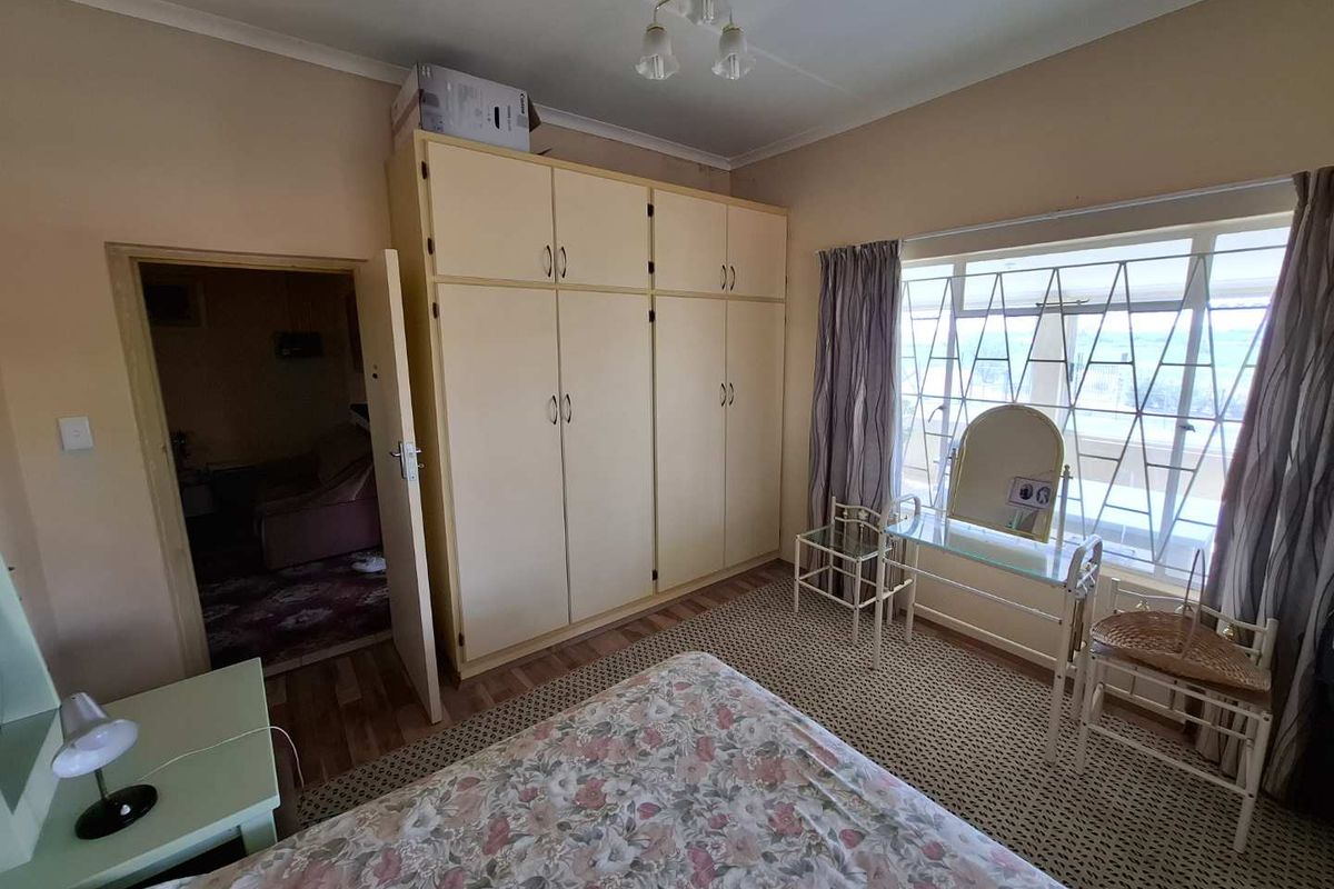 A bedroom featuring built-in cupboards, large windows with security bars, and carpeted flooring, providing a functional and well-lit living space.