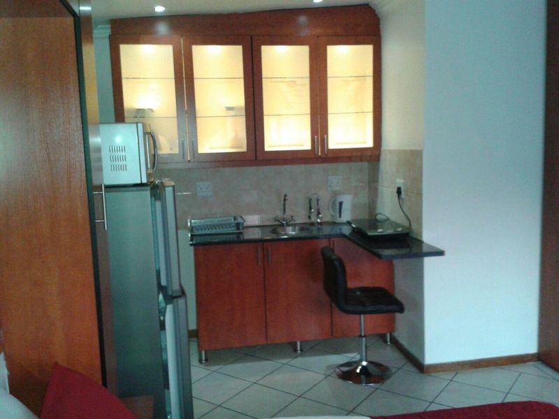 Compact kitchenette featuring wooden cabinetry, granite countertops, integrated sink, and glass-fronted upper cabinets with internal lighting.