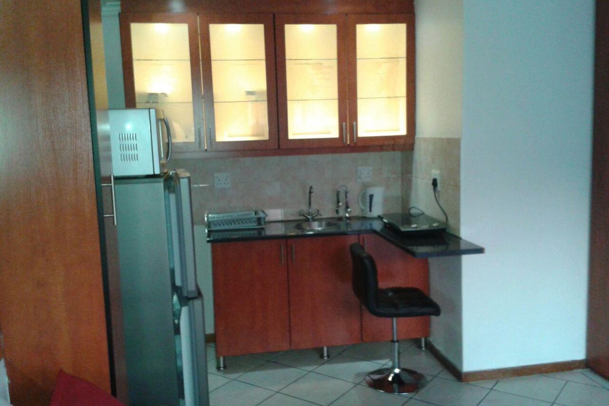 Compact kitchenette featuring wooden cabinetry, granite countertops, integrated sink, and glass-fronted upper cabinets with internal lighting.
