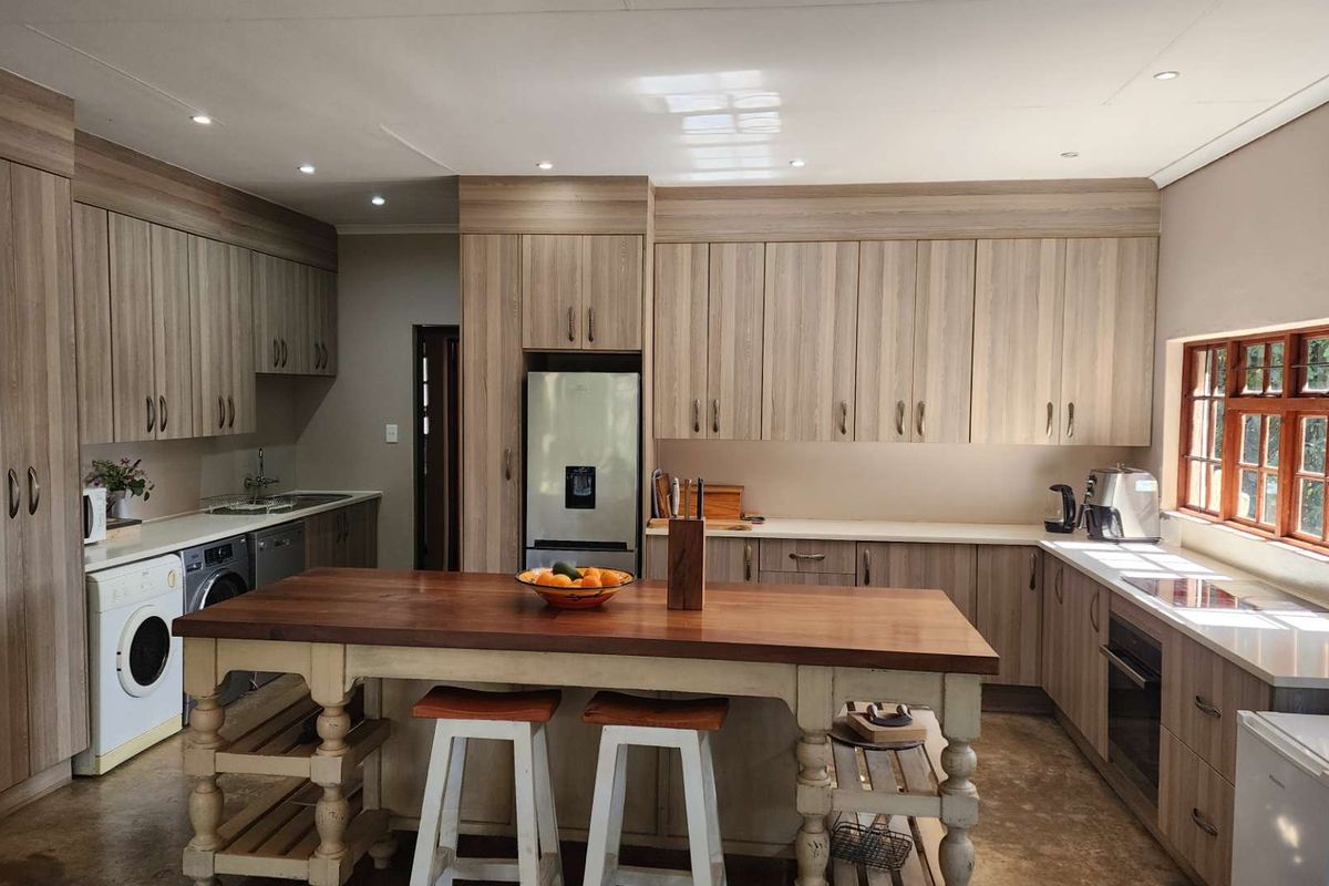 A modern, well-appointed kitchen featuring light wood-grain cabinetry, stone countertops, integrated appliances, and a central wooden island with breakfast seating.