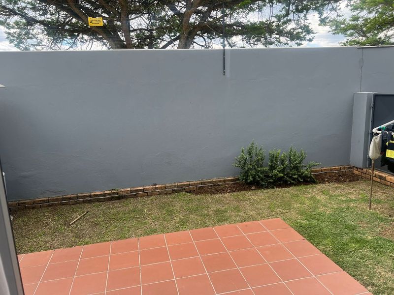 A private rear courtyard featuring a tiled patio area, a small lawn, and a solid boundary wall.