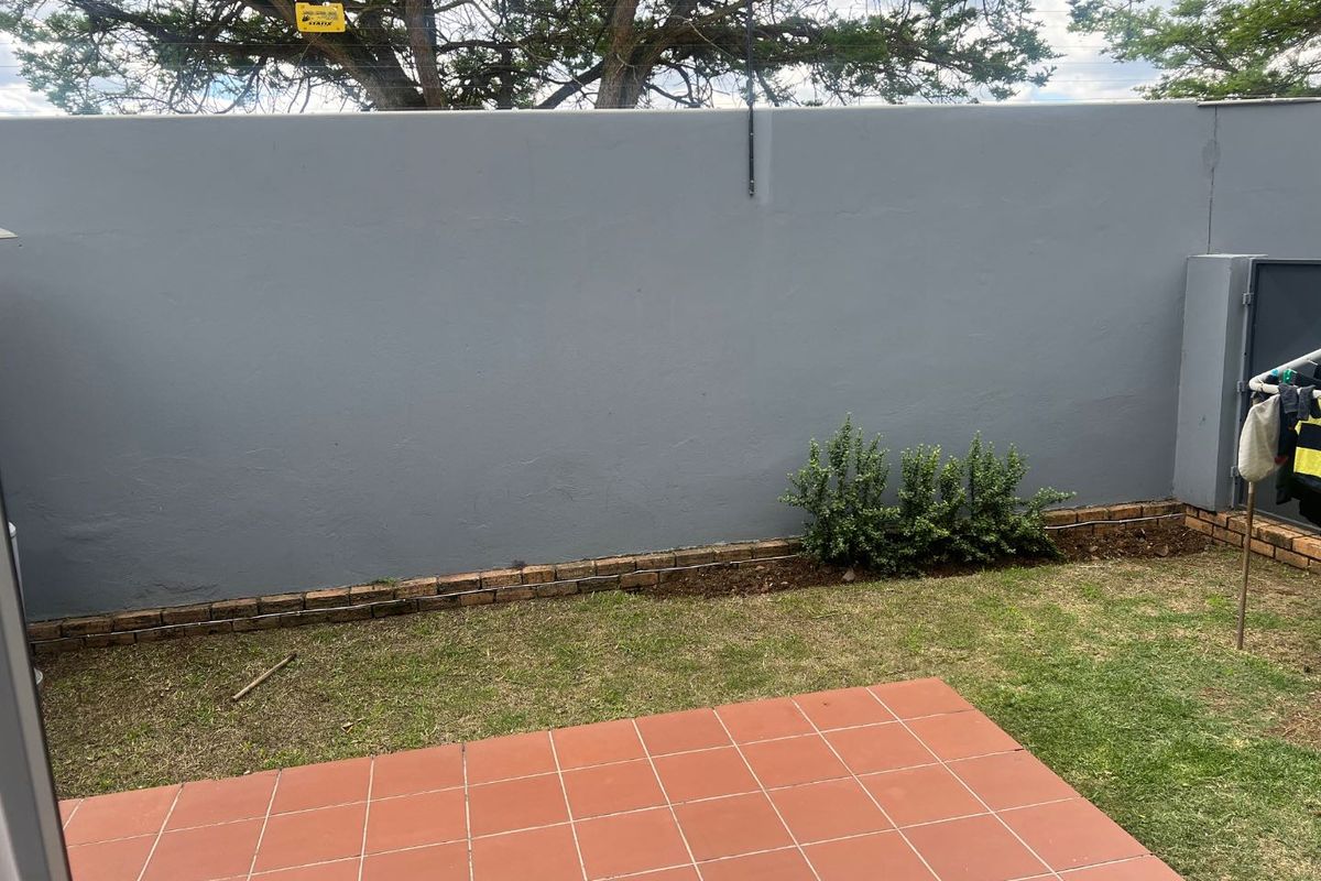 A private rear courtyard featuring a tiled patio area, a small lawn, and a solid boundary wall.