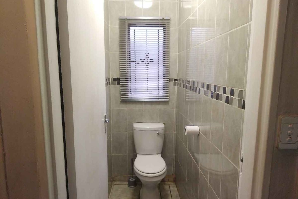 A compact guest toilet featuring floor-to-ceiling wall tiling, a standard white toilet suite, and a window with fitted blinds.