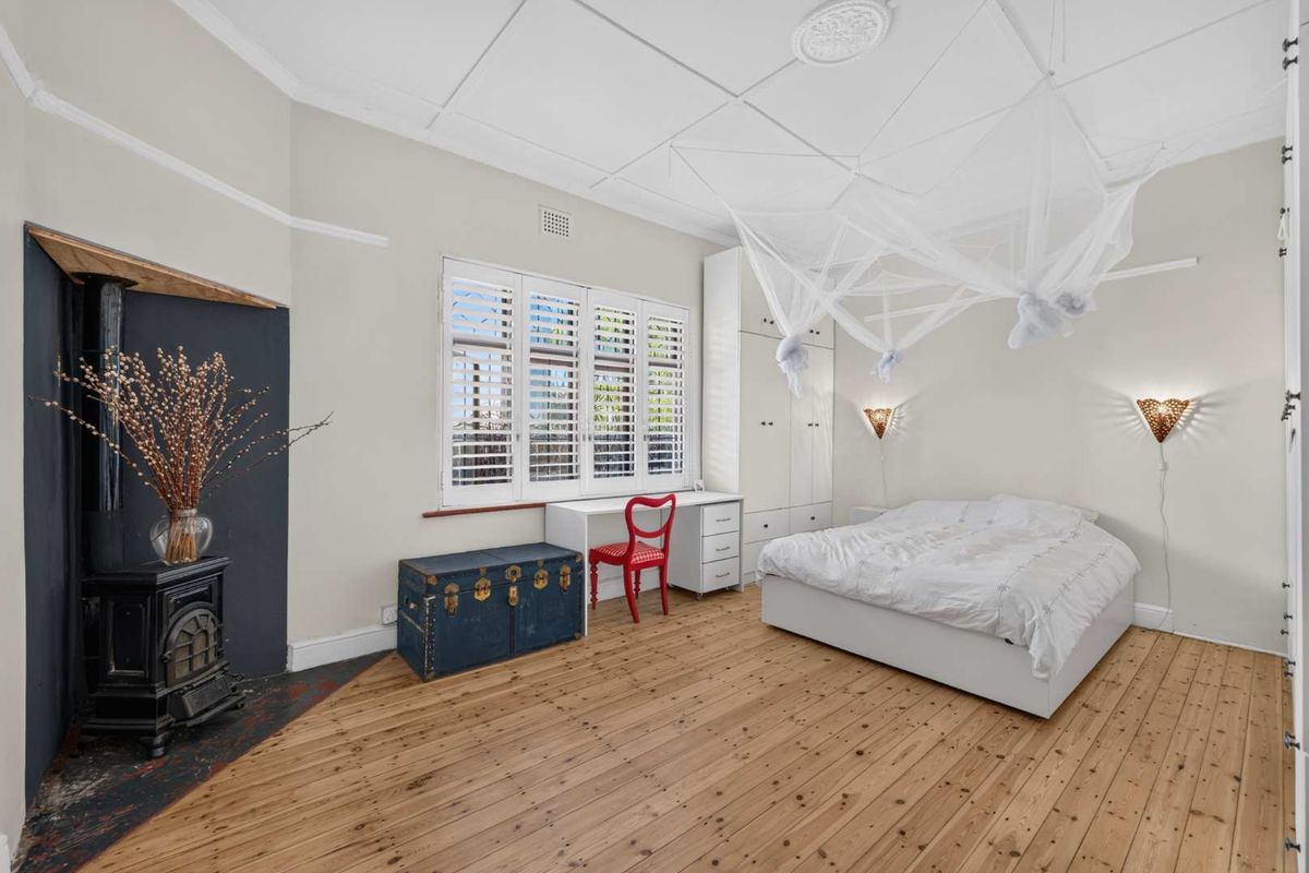 Spacious bedroom featuring original timber floorboards, a cast iron fireplace, built-in wardrobe storage, and plantation shutters.