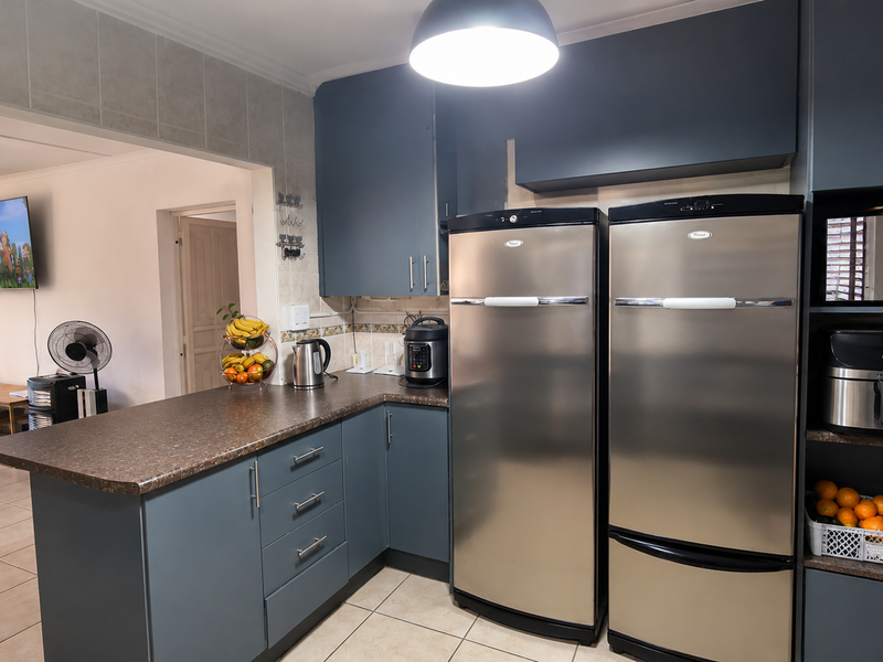 A functional kitchen featuring dark blue cabinetry, laminate countertops, tiled backsplash, and tiled flooring, with an open-plan layout connecting to the living area.