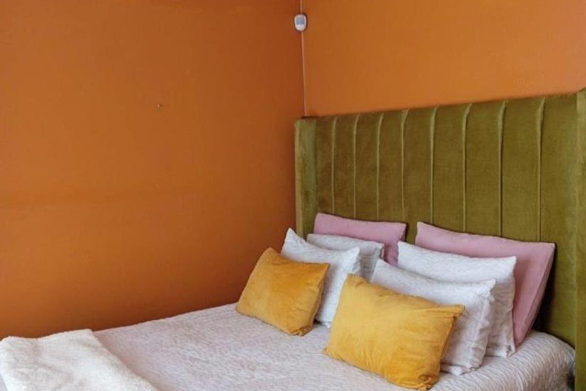 A bedroom featuring orange painted walls and a green upholstered headboard.