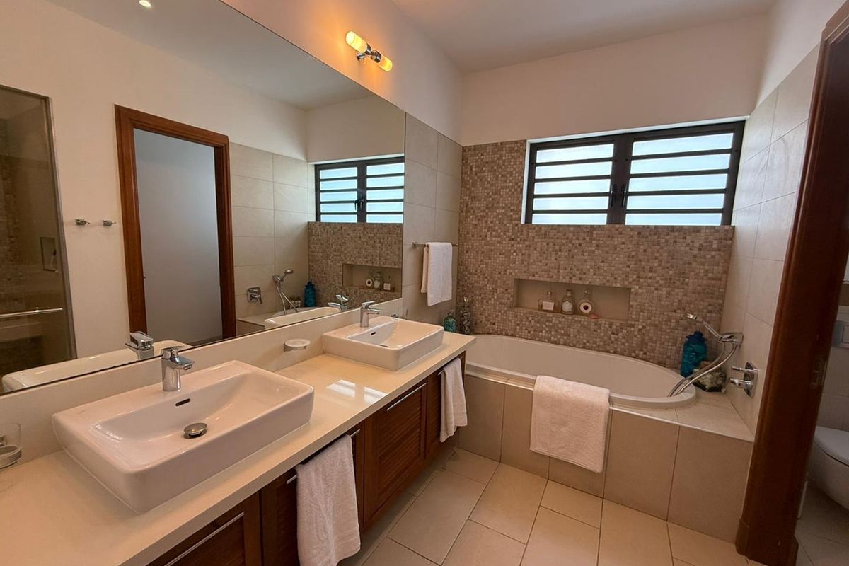 Modern bathroom featuring a double vanity with vessel sinks, a built-in bathtub with mosaic tile surround, and a large wall-to-wall mirror.