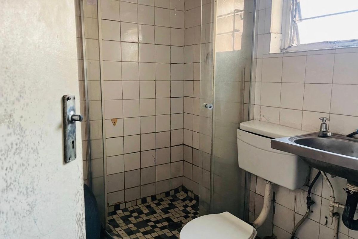 A dated bathroom featuring a shower enclosure, toilet, and wall-mounted basin, requiring significant renovation and modernization of finishes and fixtures.