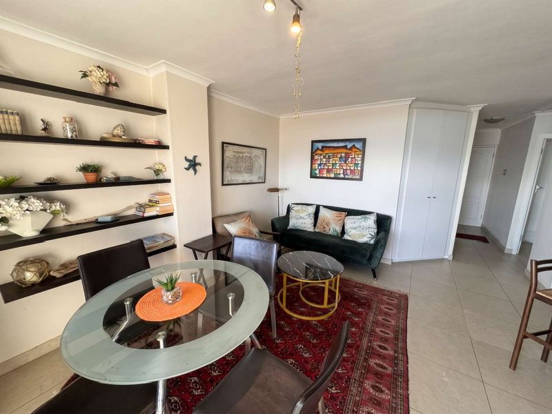 An open-plan living and dining area featuring tiled flooring, built-in shelving units, and a built-in storage cupboard.