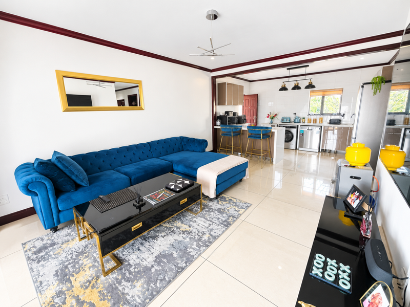 Spacious open-plan living area featuring polished floor tiles, a modern kitchen with island seating, and elegant crown molding throughout the combined space.