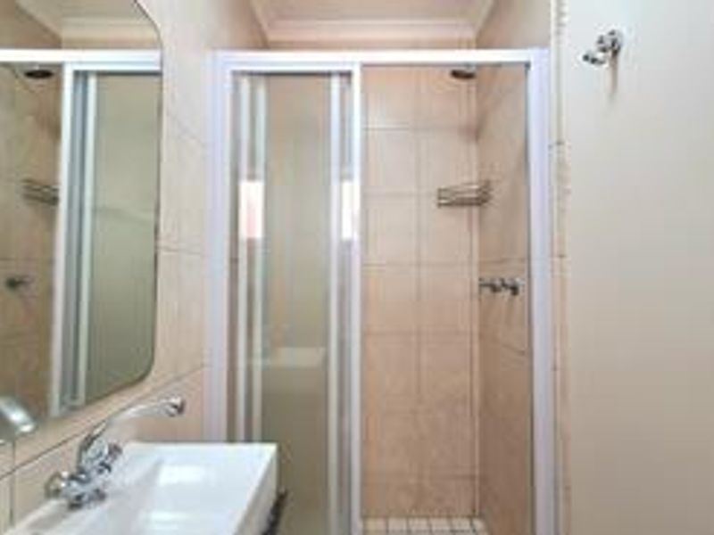 A functional bathroom featuring a tiled shower enclosure, a wall-mounted basin with a mixer tap, and a large wall mirror.